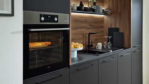 Einbauküche Interliving aus Holz in Schwarz Interliving Küche Serie 3103 mit AEG Einbaugeräten Mattschwarz & Vulkaneiche  - dreizeilig